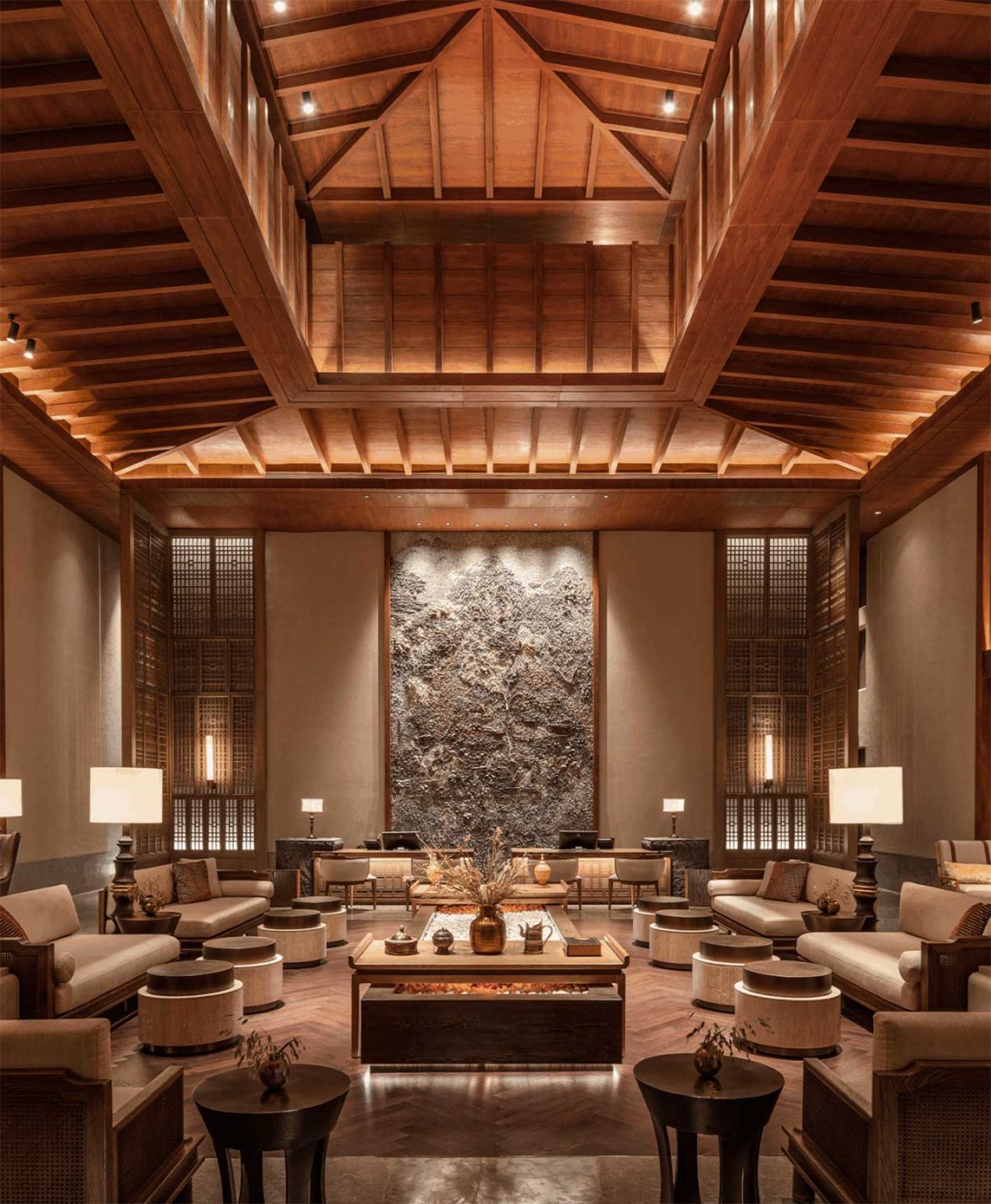 Luxurious hotel lobby with high wooden ceilings, plush seating, and warm lighting. A large, textured wall art centerpiece adds elegance. Cozy and inviting.
