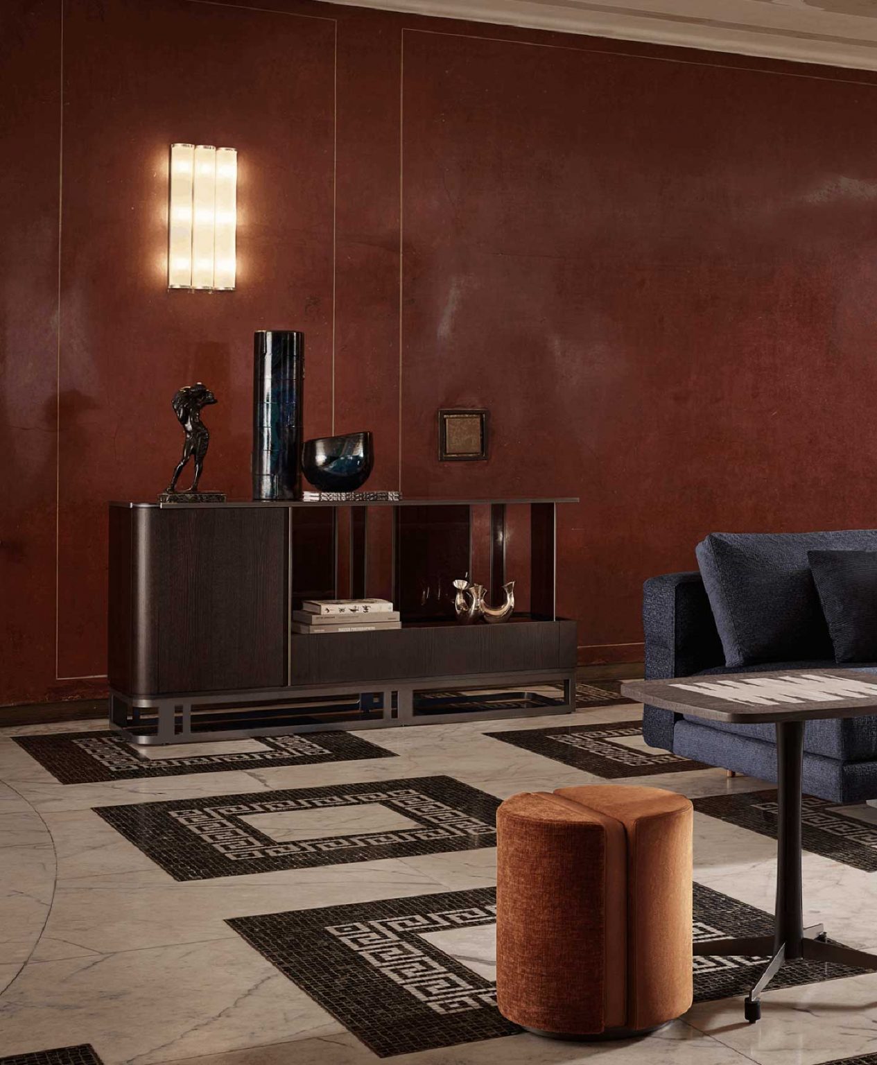 Luxurious living room with red walls, a sleek modern sideboard with dark wood finish, a navy sofa adorned with orange pillows and a throw, elegant lighting, and marble stairs. Sophisticated and warm.