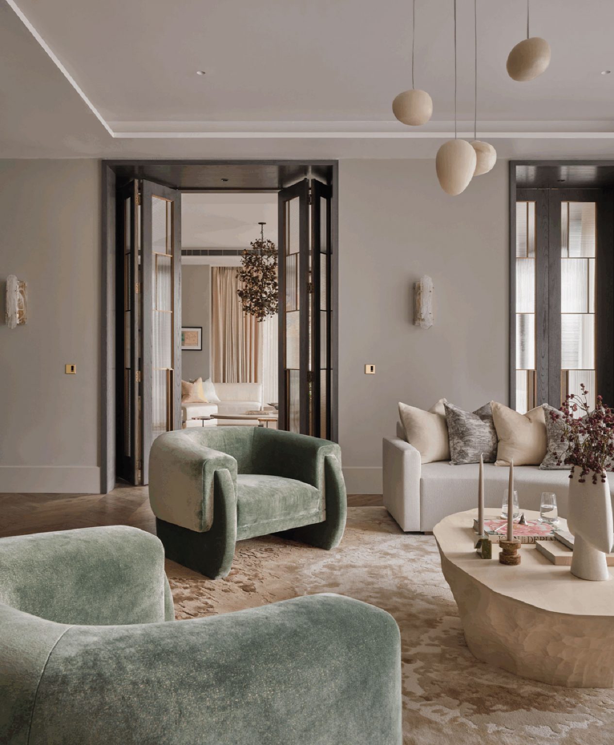 Elegant living room with sage green armchairs, beige sofa, and modern decor. Open double doors lead to another room, creating an airy, sophisticated feel.